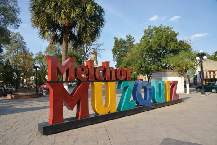 Vista de la plaza principal de Melchor Múzquiz, con su iglesia colonial y árboles.